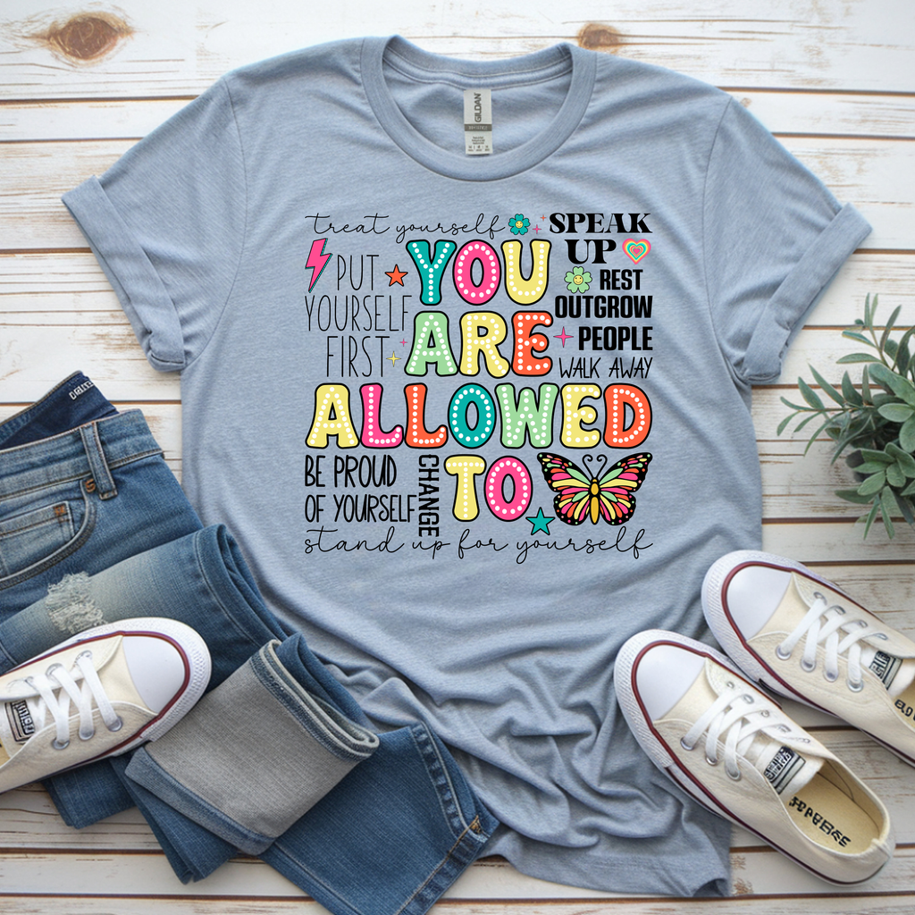 You Are Allowed To graphic t-shirt featuring colorful affirmations on a light blue background, styled with jeans and sneakers.